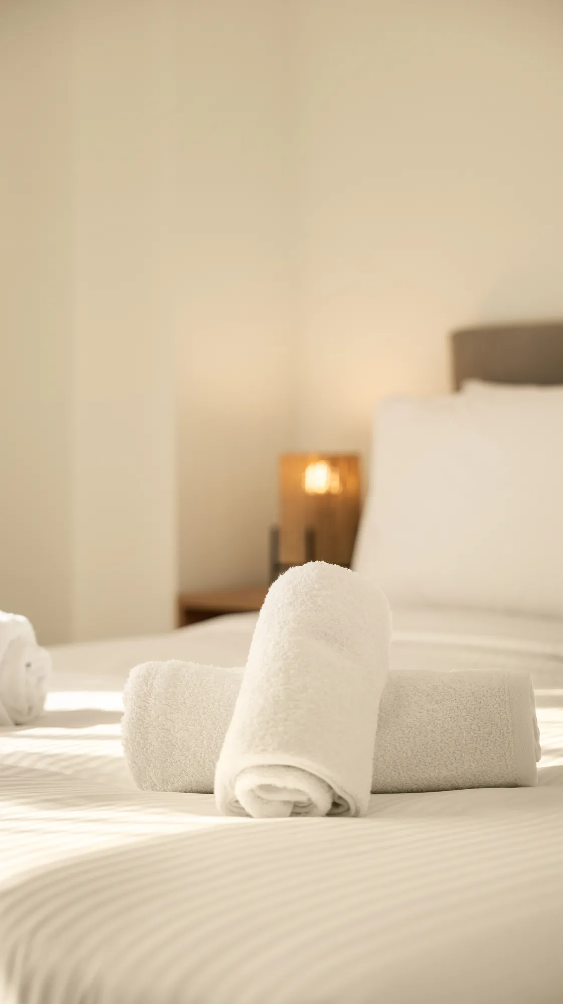 ORMOS Piraeus, rolled towels on a made bed in soft light