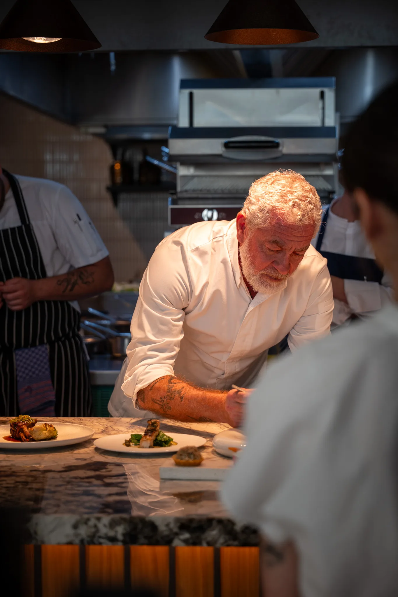 The chef leaning over the pass to finish a plate
